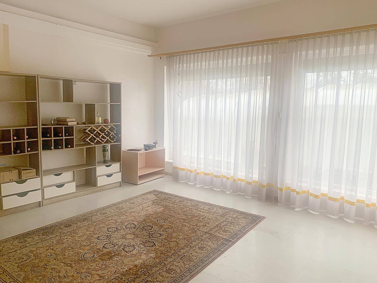 Heller Raum mit großen Fenstern, Teppich und Regalsystemen für Lagerung oder Dekoration.