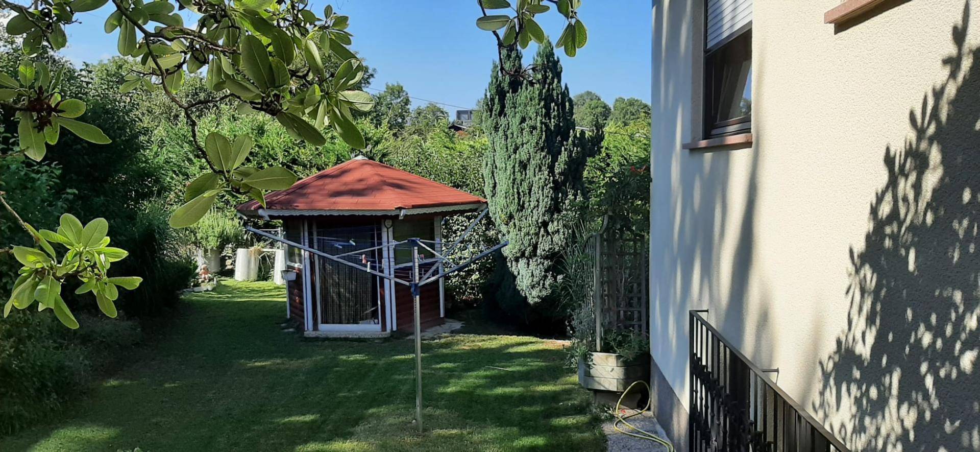 Idyllischer Garten mit einem roten Gartenpavillon, umgeben von Bäumen und Sträuchern.