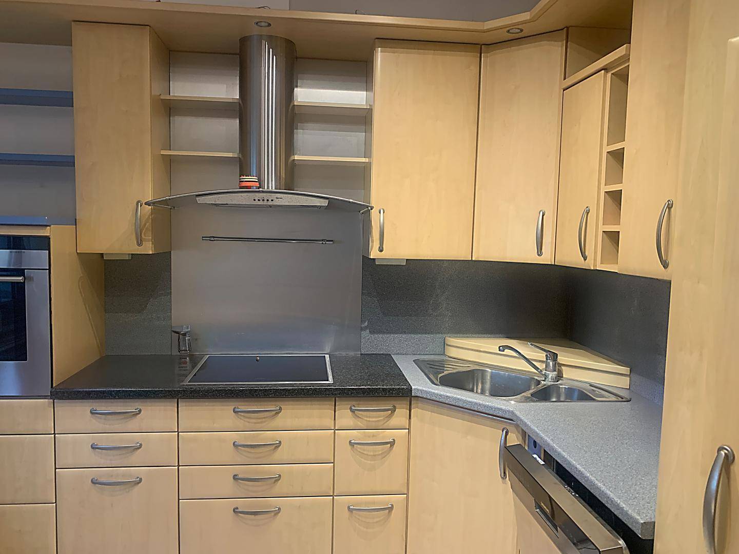 Funktionale Küche mit hellen Holzschränken, Edelstahlgeräten und dunkler Arbeitsplatte.