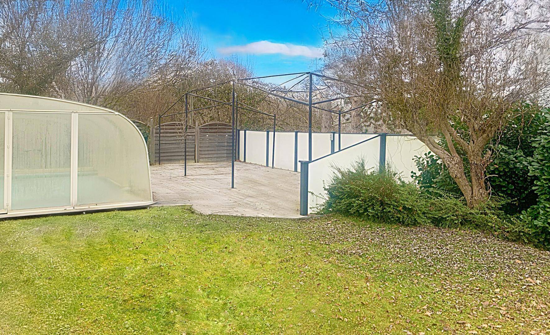 Großer Gartenbereich mit Rasenfläche, Bäumen und einer Metallkonstruktion für eine Pergola oder Überdachung.