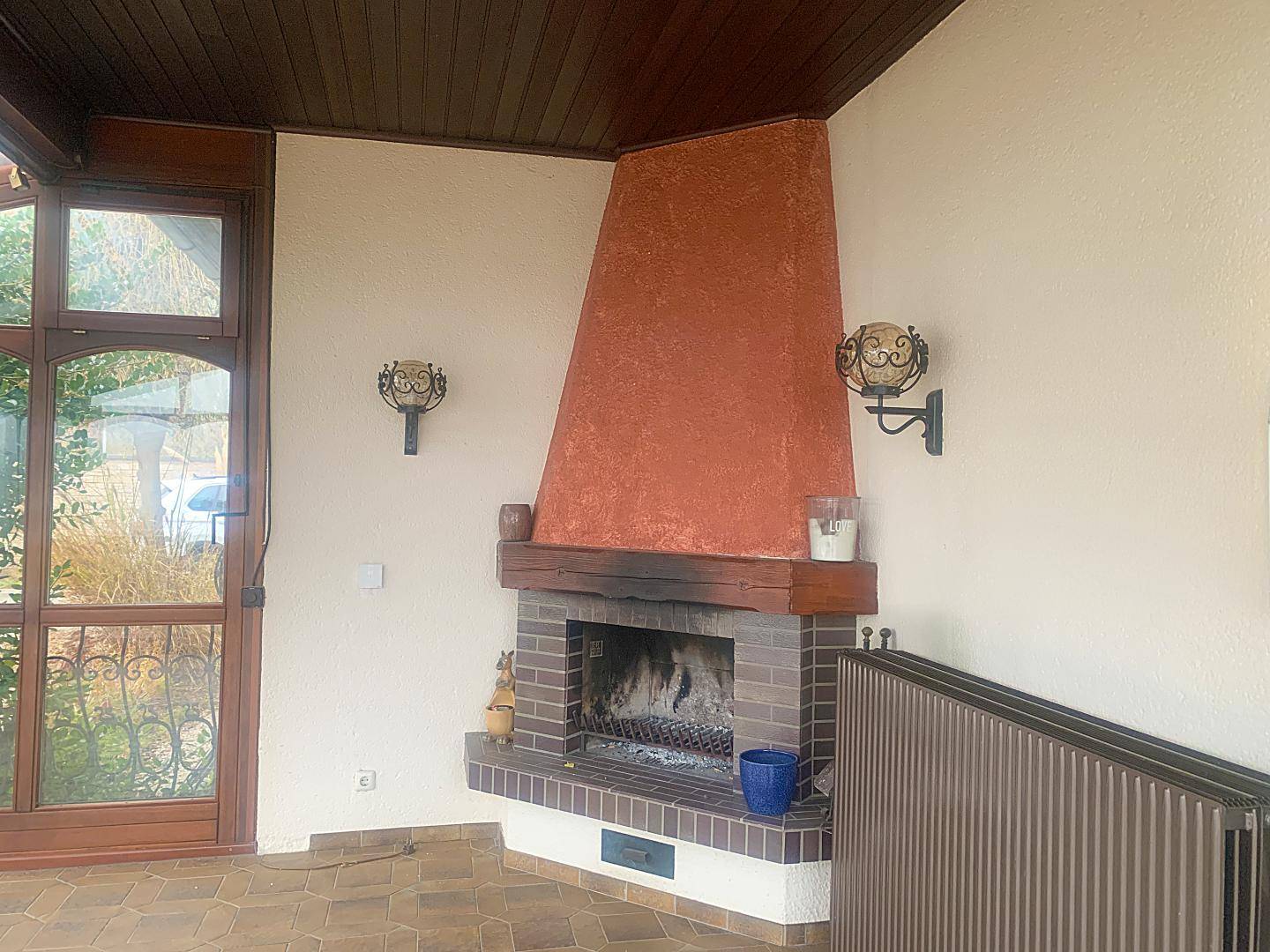 Verglaster Wintergarten mit Kamin, Fliesenboden und rustikalen Wandleuchten.