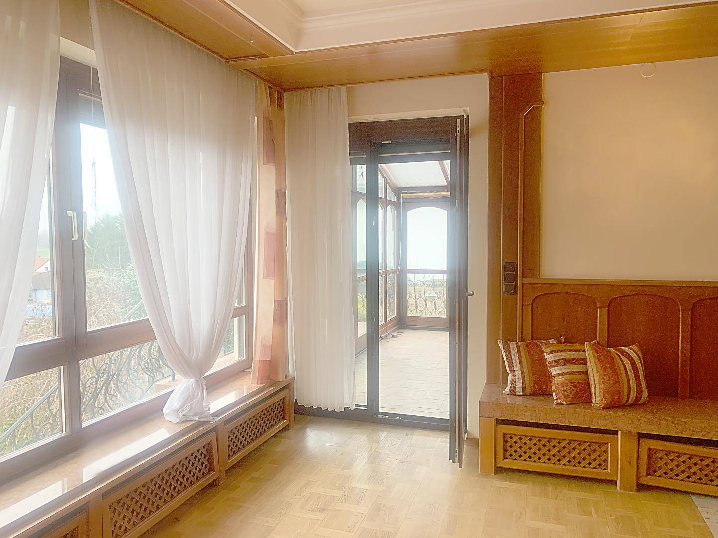 Wohnzimmer mit Parkettboden, Holzvertäfelung und direktem Zugang zum verglasten Wintergarten.