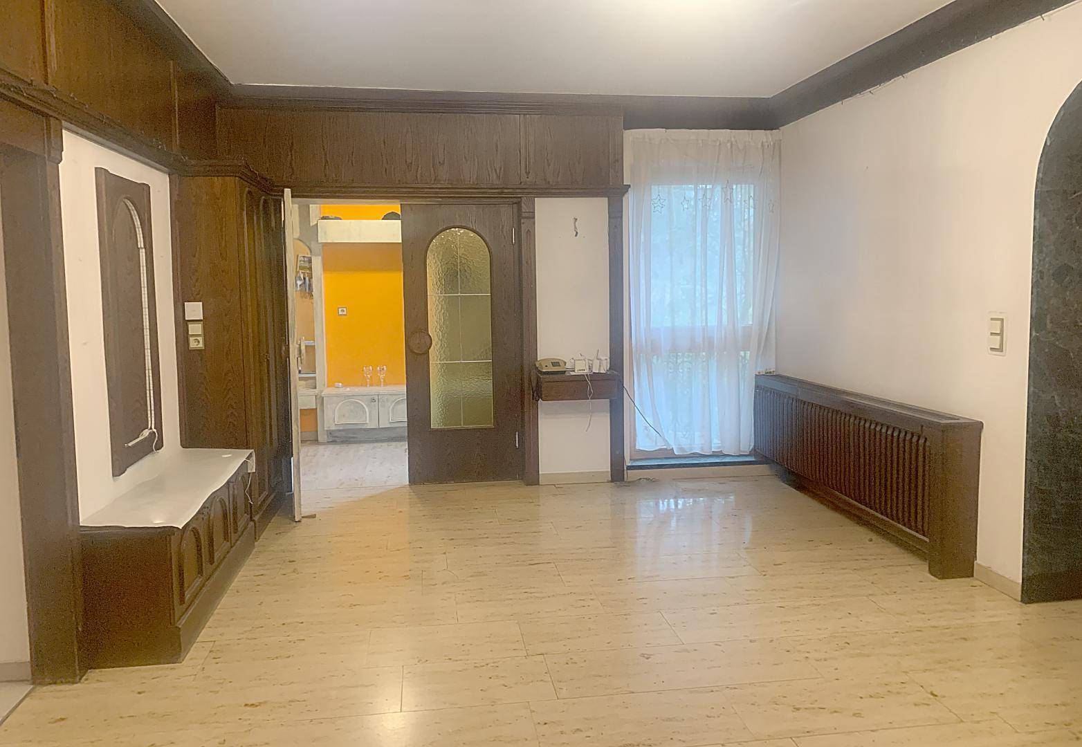 Geräumiger Innenraum mit Fliesenboden, Holzvertäfelung und Zugang zu weiteren Zimmern.