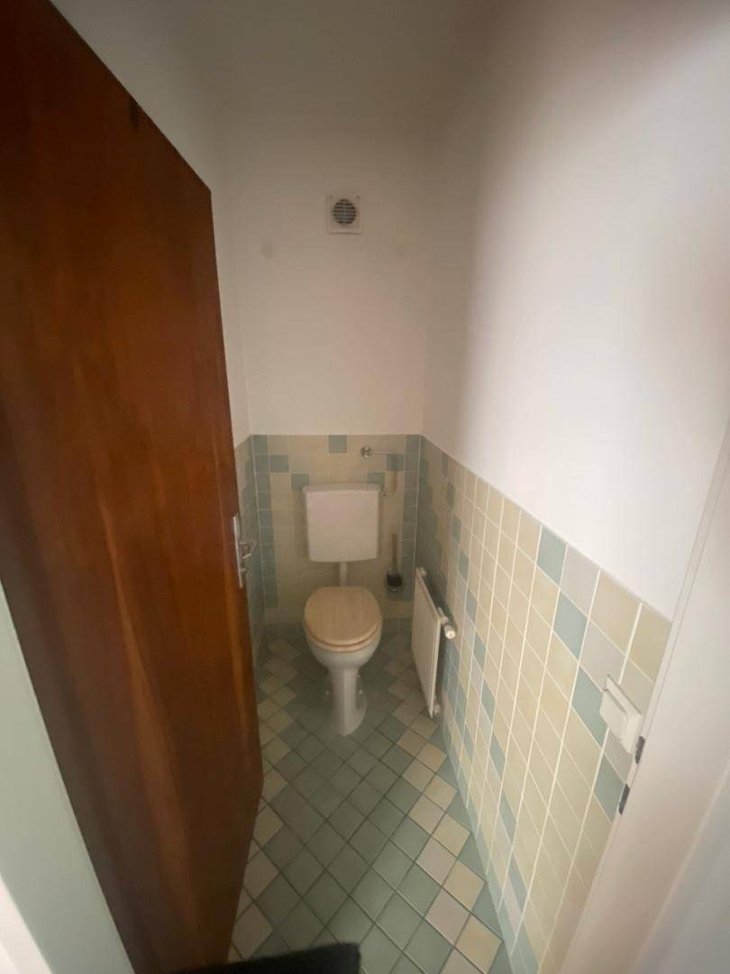 Separate Gästetoilette mit hellblauen und beigen Fliesen sowie einem kleinen Heizkörper.