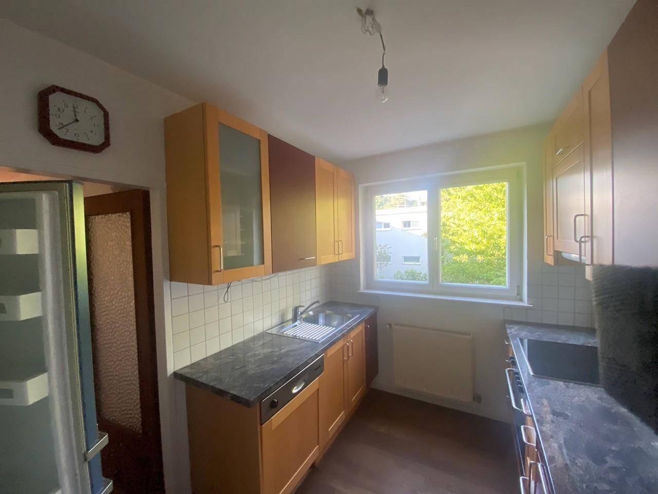 Helle Küche mit Holzschränken, dunkler Arbeitsplatte und einem Fenster mit Blick ins Grüne.