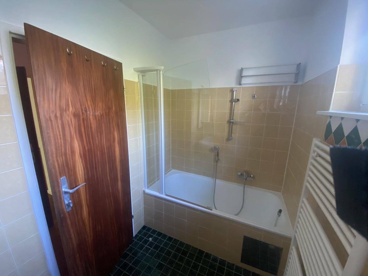 Badezimmer mit Badewanne, Duschabtrennung, beigen Fliesen und einem beheizten Handtuchhalter.