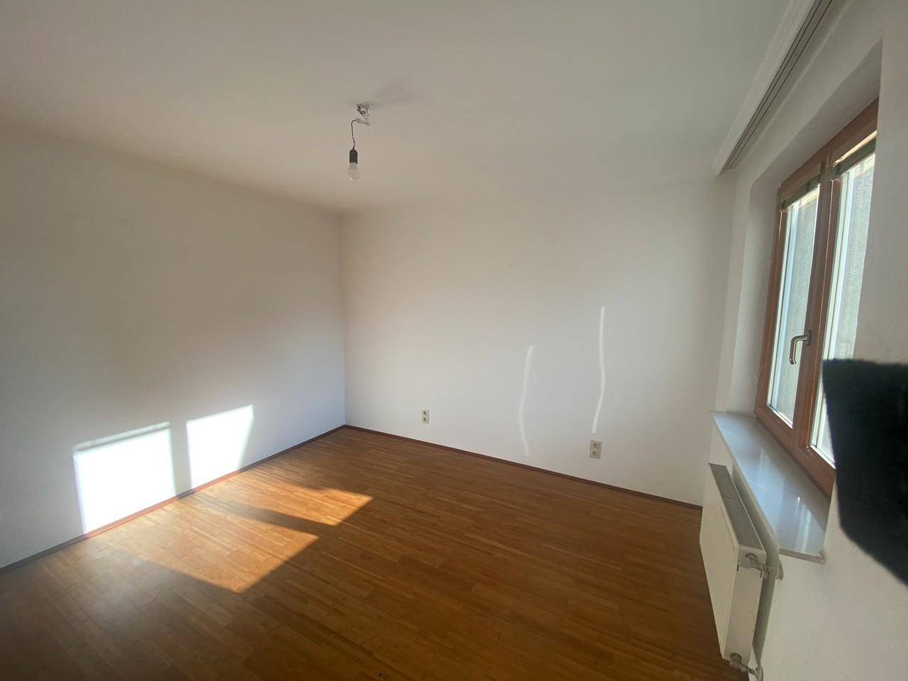Geräumiges Zimmer mit Holzboden und Fenster, das viel Sonnenlicht in den Raum bringt.