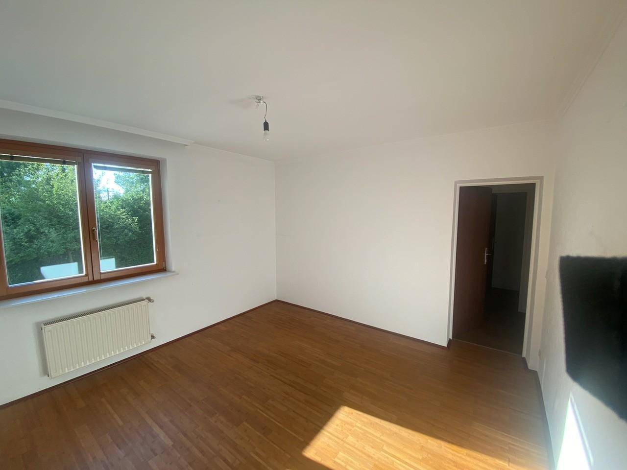 Helles Zimmer mit Parkettboden und großem Fenster, das viel Tageslicht hereinlässt.