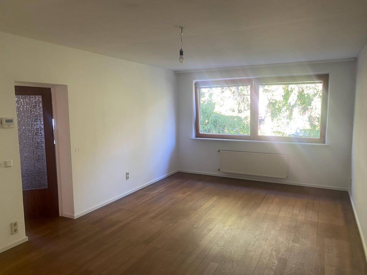 Heller Wohnraum mit Parkettboden und großen Fenstern, die einen Blick ins Grüne bieten.