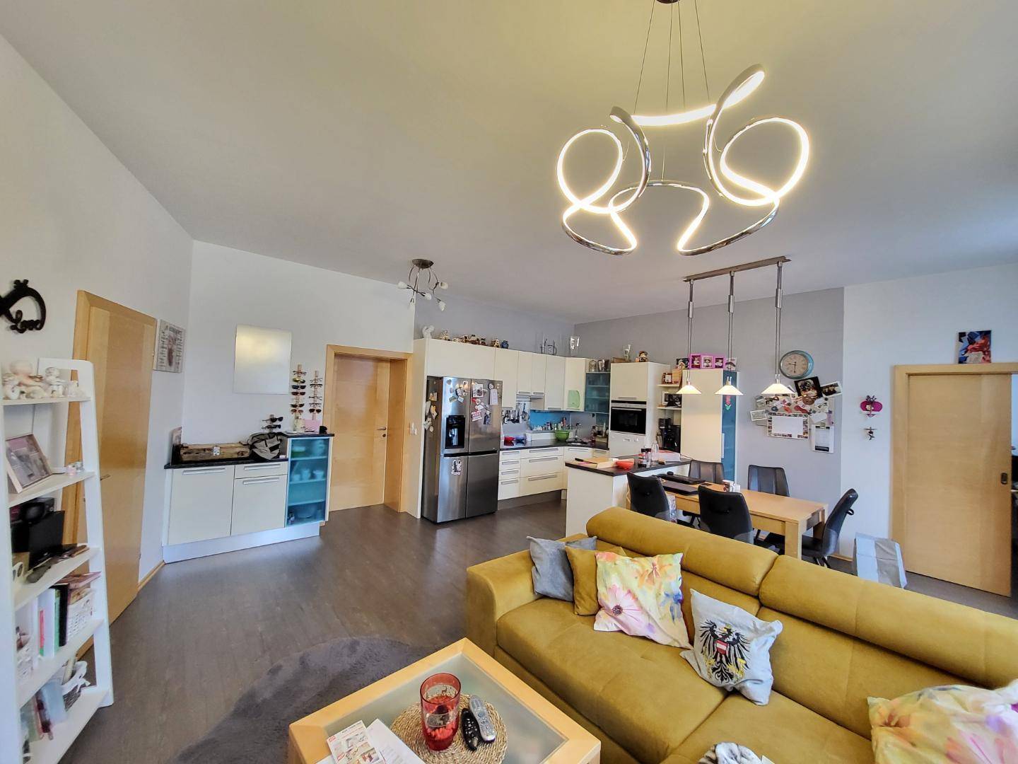 Geräumiger offener Wohnbereich mit moderner Küche, Essbereich und gemütlichem Sofa unter einer Designerlampe.