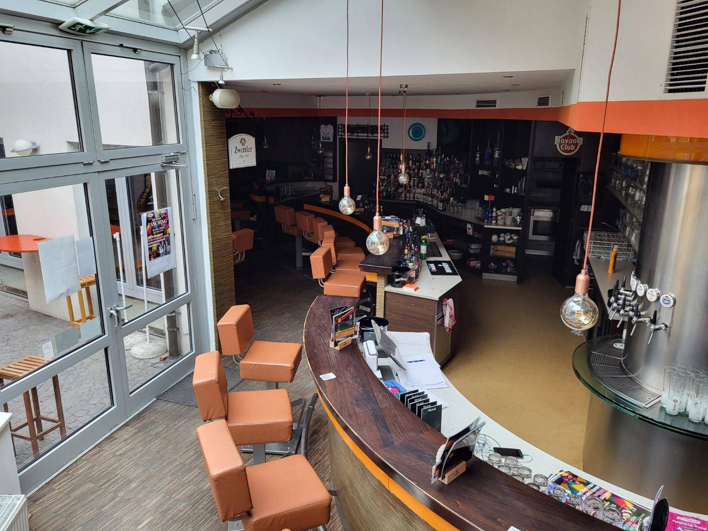 Moderne Bar mit geschwungener Theke, hohen Hockern und großen Glasfronten, die viel Licht hereinlassen.
