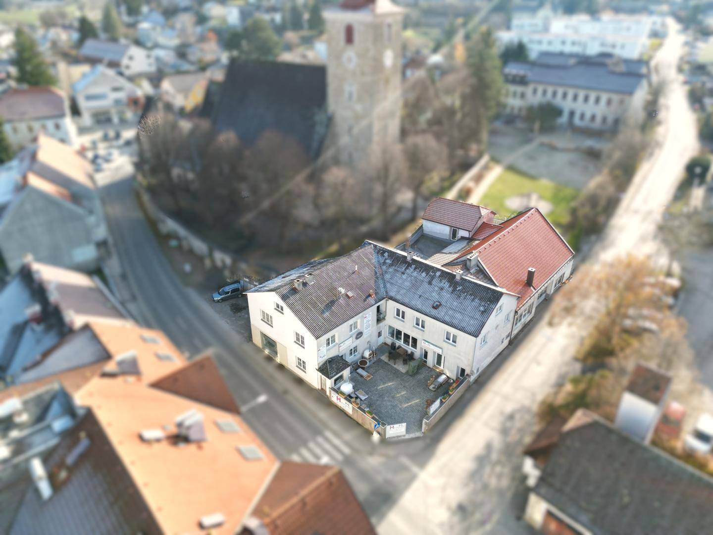 Übersicht des Gebäudekomplexes aus der Vogelperspektive mit angrenzender Kirche und umliegender Bebauung.