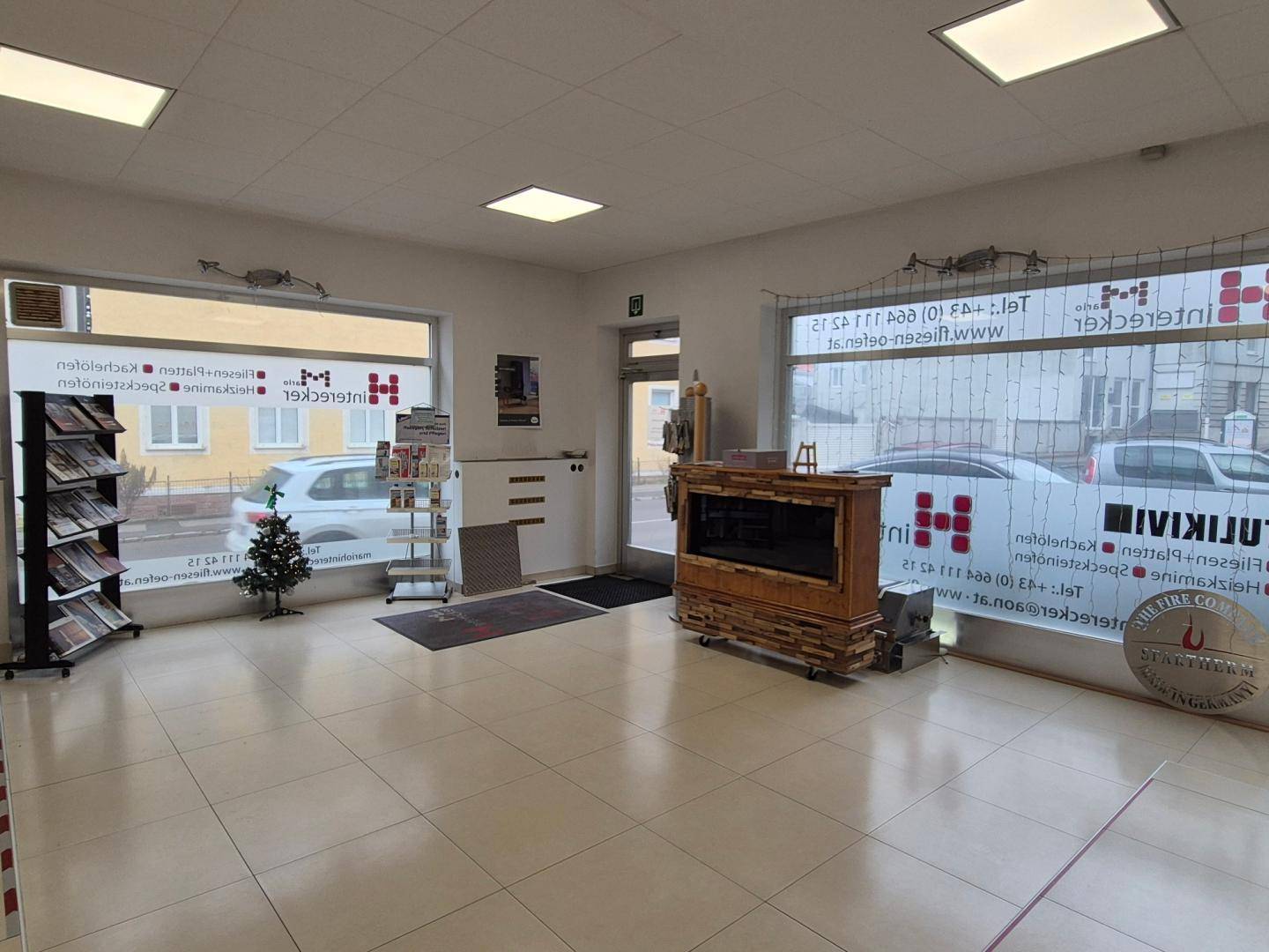 Heller Verkaufsraum mit großen Schaufenstern, Fliesenboden und Ausstellungsstücken für Kamine.