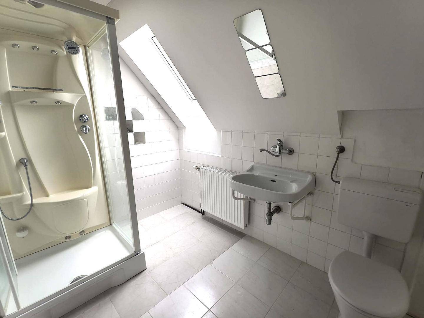 Dachgeschoss-Badezimmer mit Duschkabine, Waschbecken und Toilette unter einer Dachschräge.