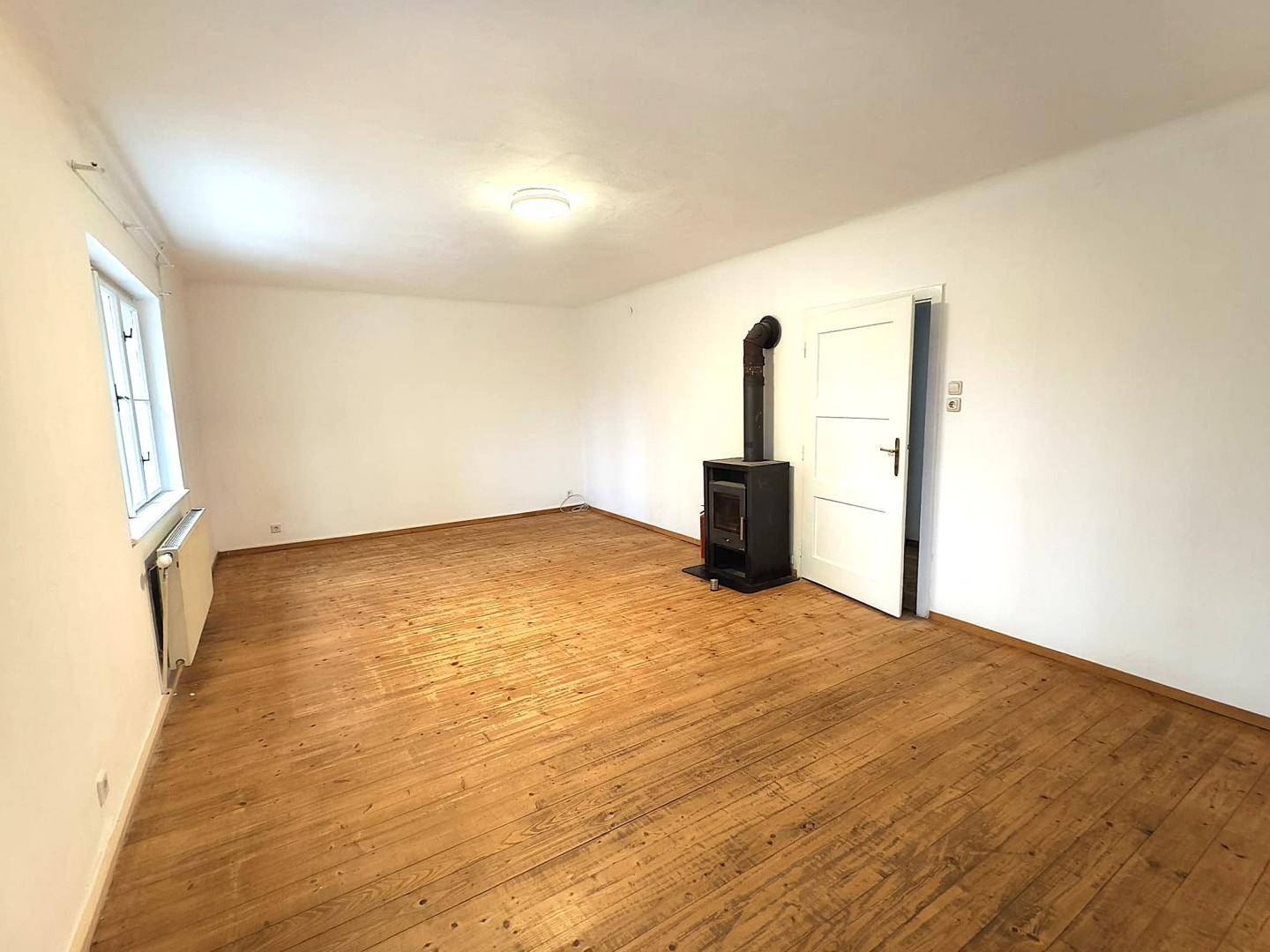 Geräumiges Wohnzimmer mit Holzboden und einem modernen Holzofen, der Wärme spendet.