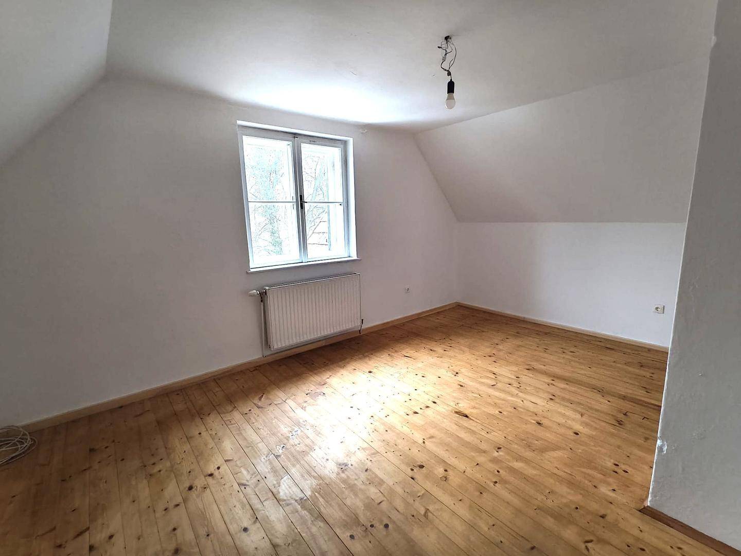 Helles Schlafzimmer im Dachgeschoss mit Holzboden, Dachschräge und Blick ins Grüne.