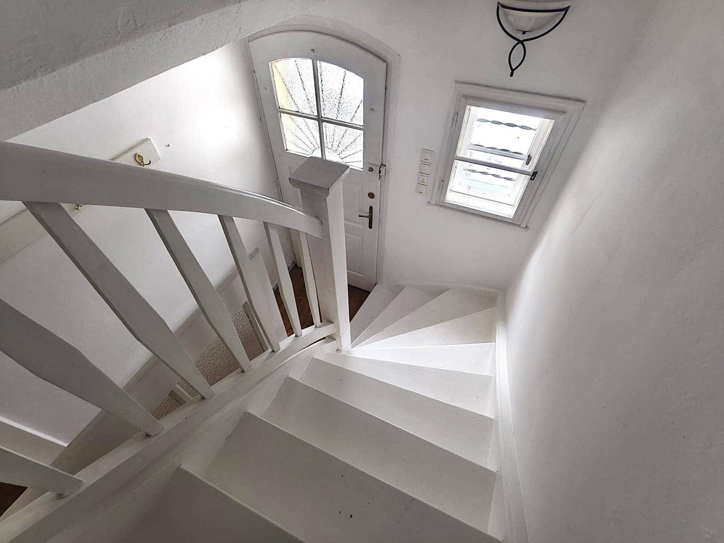 Weiß gestrichenes Treppenhaus mit Holzgeländer und einer charmanten Eingangstür mit Glasfenstern.