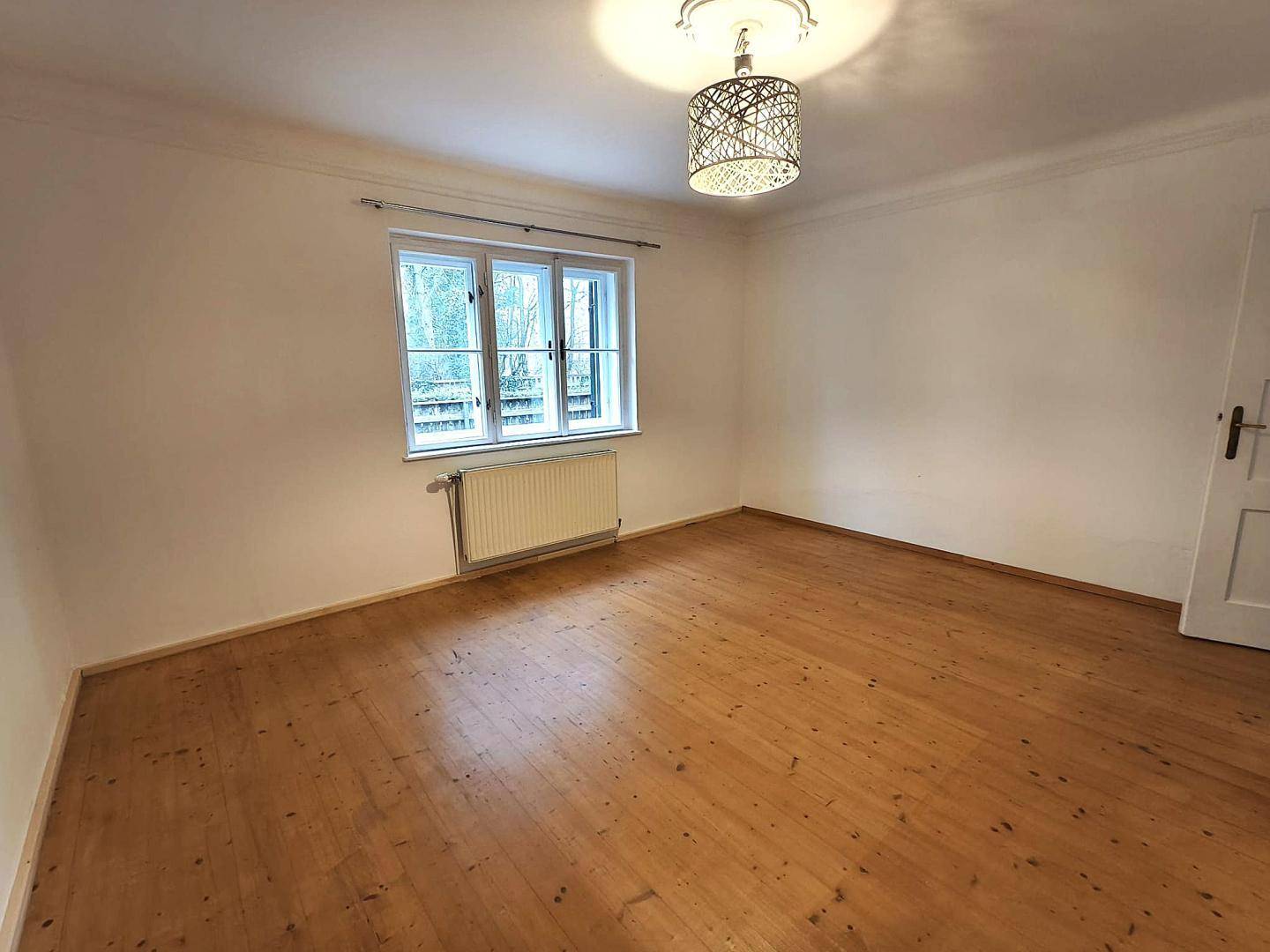 Gemütliches Zimmer mit Holzboden, großen Fenstern und einer dekorativen Deckenleuchte.
