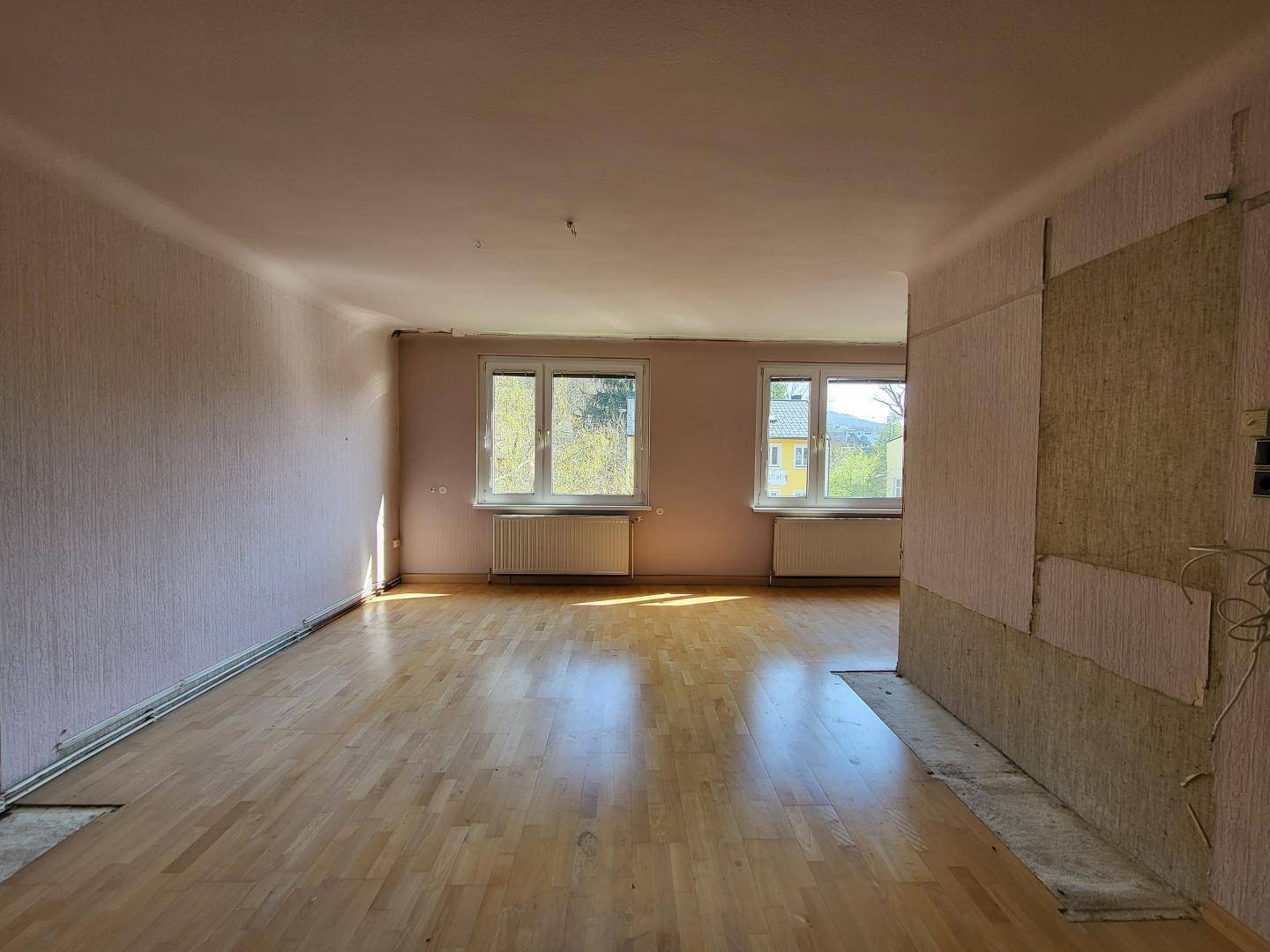 Helles Wohnzimmer mit Parkettboden und Blick ins Grüne, ideal für eine moderne Umgestaltung.