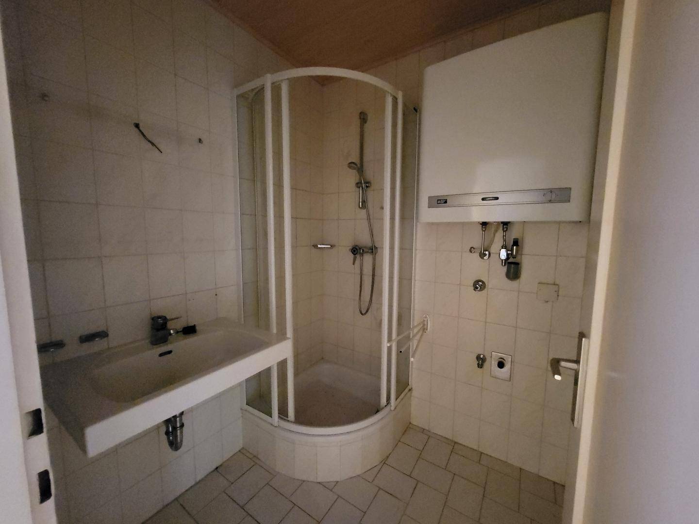 Badezimmer mit Duschkabine, Waschbecken und Gastherme, benötigt eine Modernisierung.
