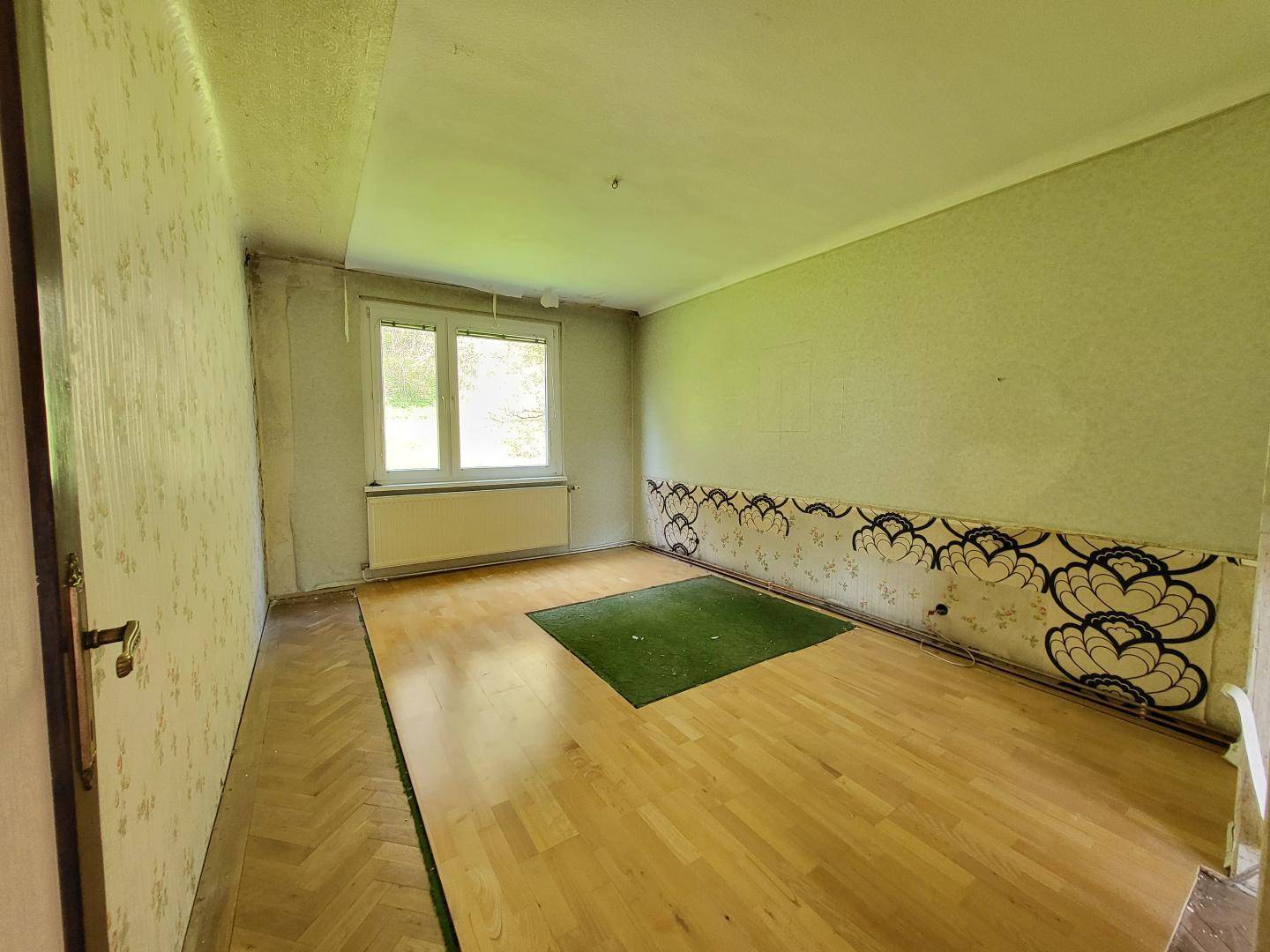 Schlafzimmer mit Parkettboden und Fensterblick ins Grüne, bereit für eine umfassende Renovierung.