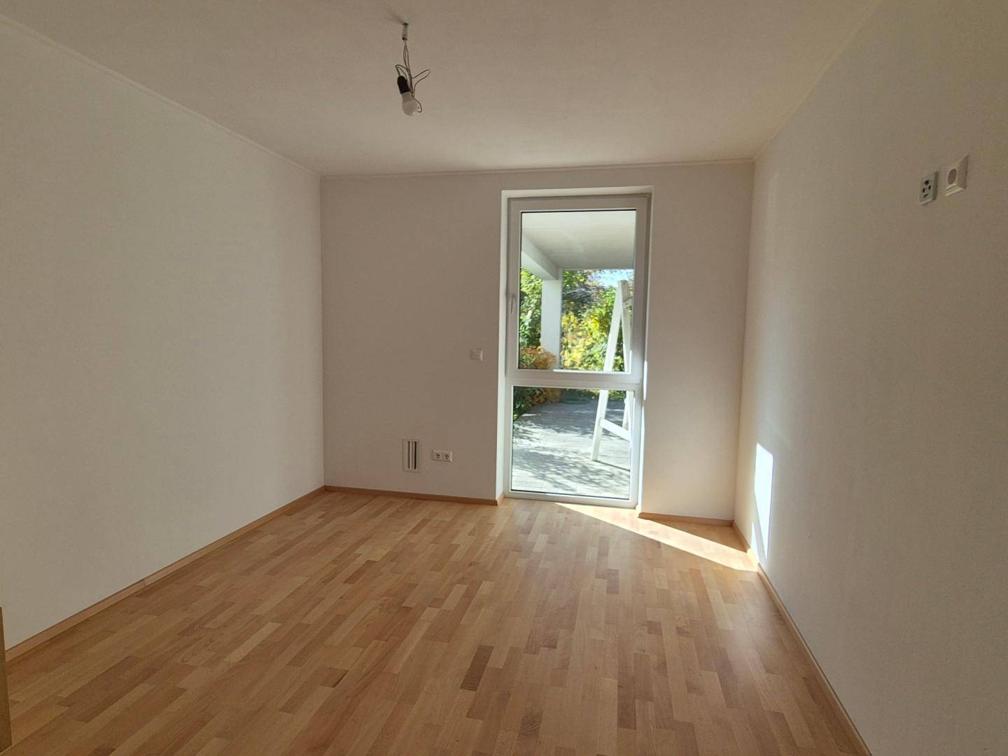 Helles Schlafzimmer mit Parkettboden und Zugang zu einem Außenbereich, ideal für Ruhe.