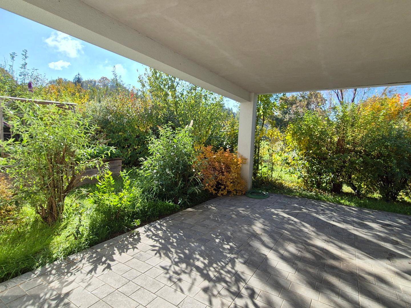 Überdachte Terrasse mit grauen Pflastersteinen und Blick ins Grüne, ideal für entspannte Stunden im Freien.
