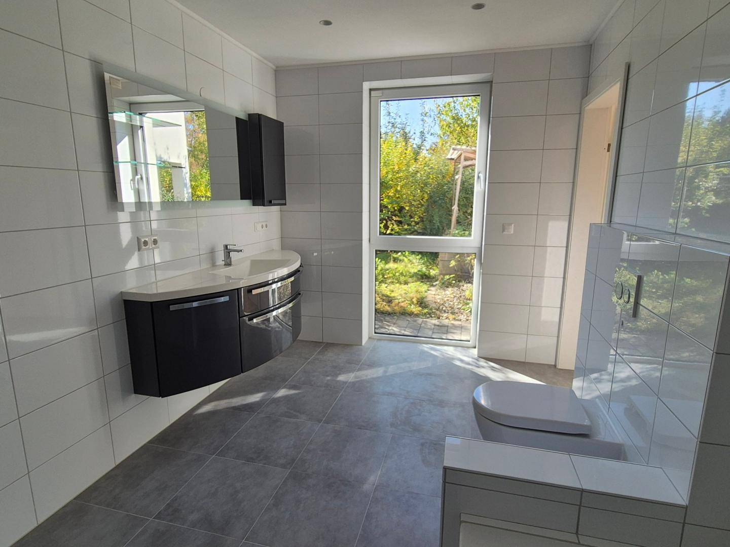 Geräumiges modernes Badezimmer mit Doppelwaschbecken, wandhängendem WC und großem Fenster zum Garten.
