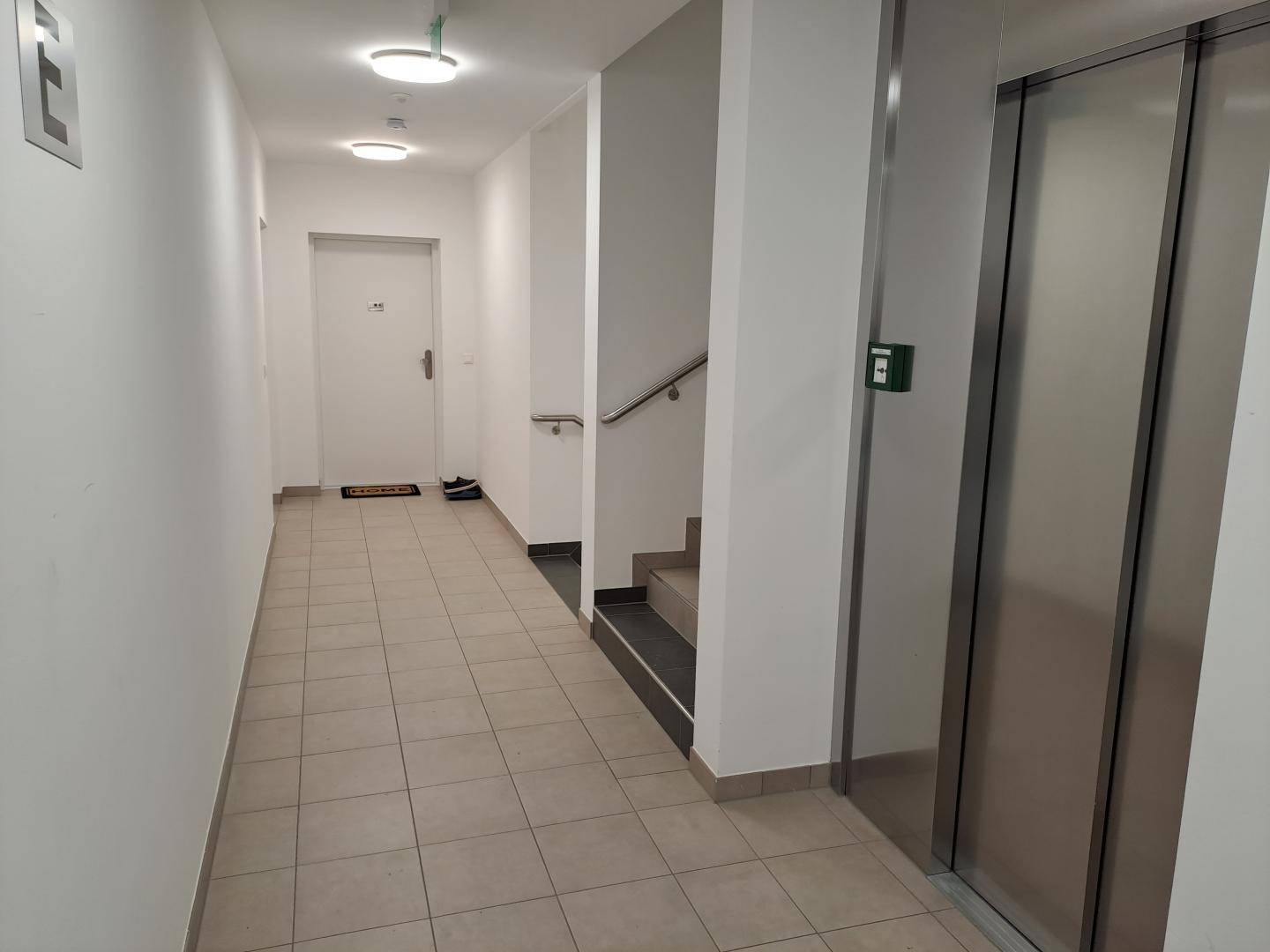 Heller Gemeinschaftsflur mit Fliesenboden, Treppe und modernem Aufzug im Gebäude.
