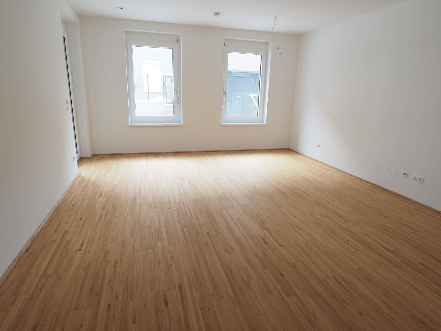 Geräumiges, helles Zimmer mit Holzboden und zwei großen Fenstern.