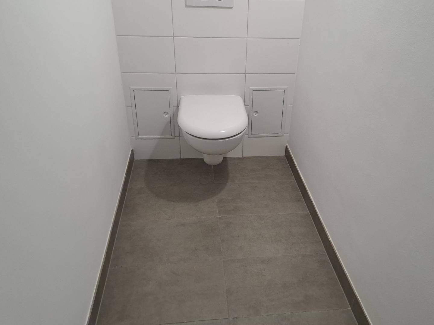Separates WC mit wandhängender Toilette und modernen Fliesen an Wänden und Boden.