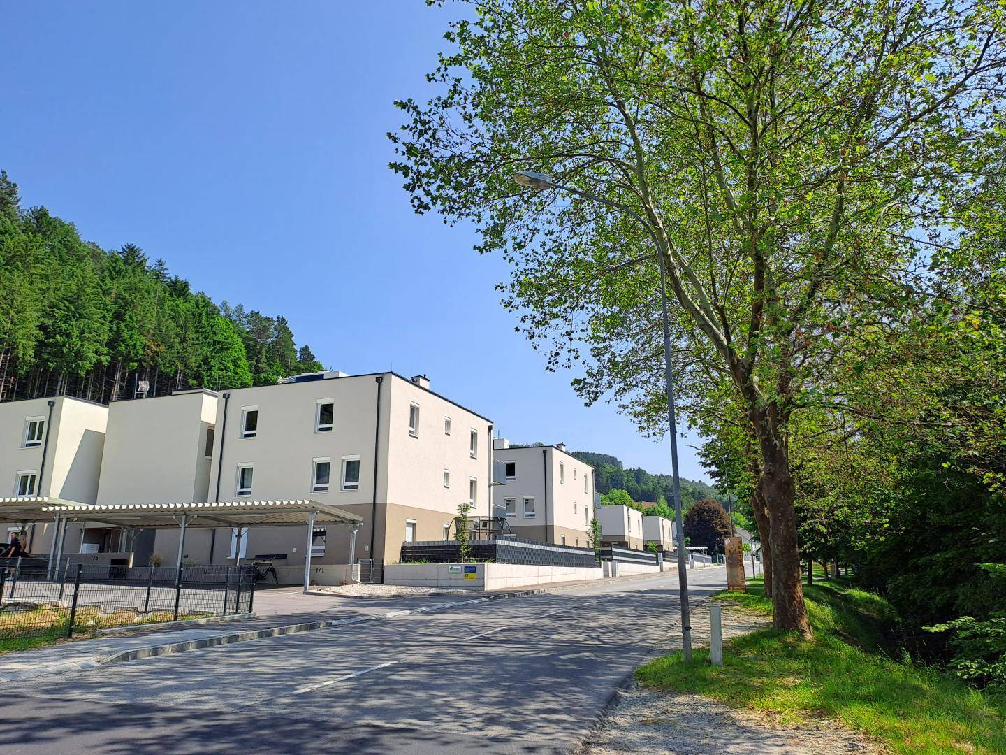 Moderne Wohngebäude mit Carports und grüner Umgebung unter blauem Himmel.
