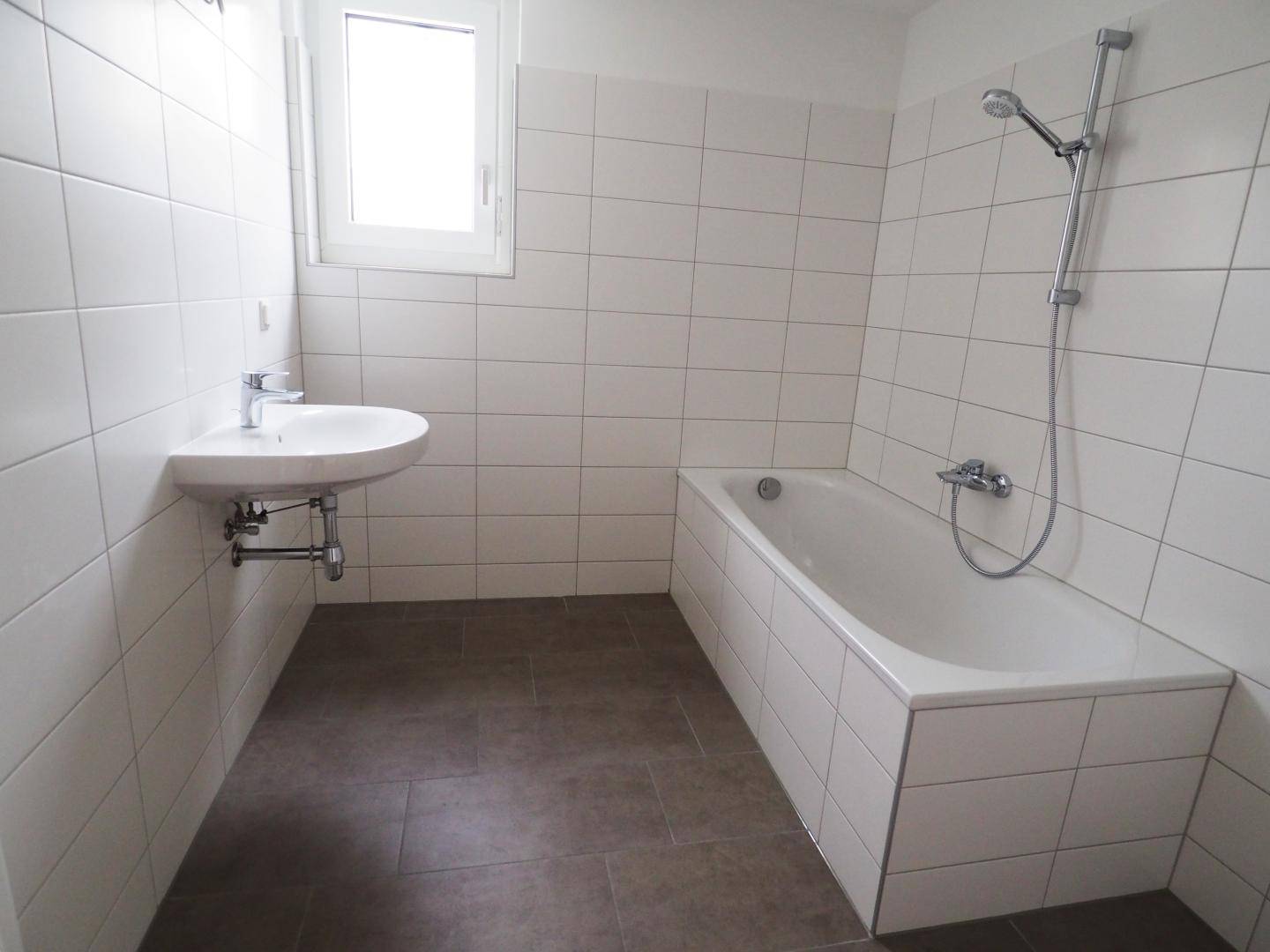 Helles Badezimmer mit Badewanne, Waschbecken und Fenster für natürliche Belüftung.