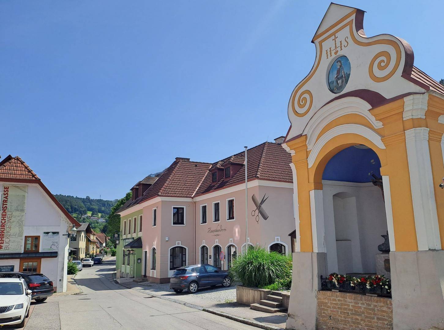 Malerische Dorfstraße mit traditionellen Gebäuden und einer kleinen Kapelle.