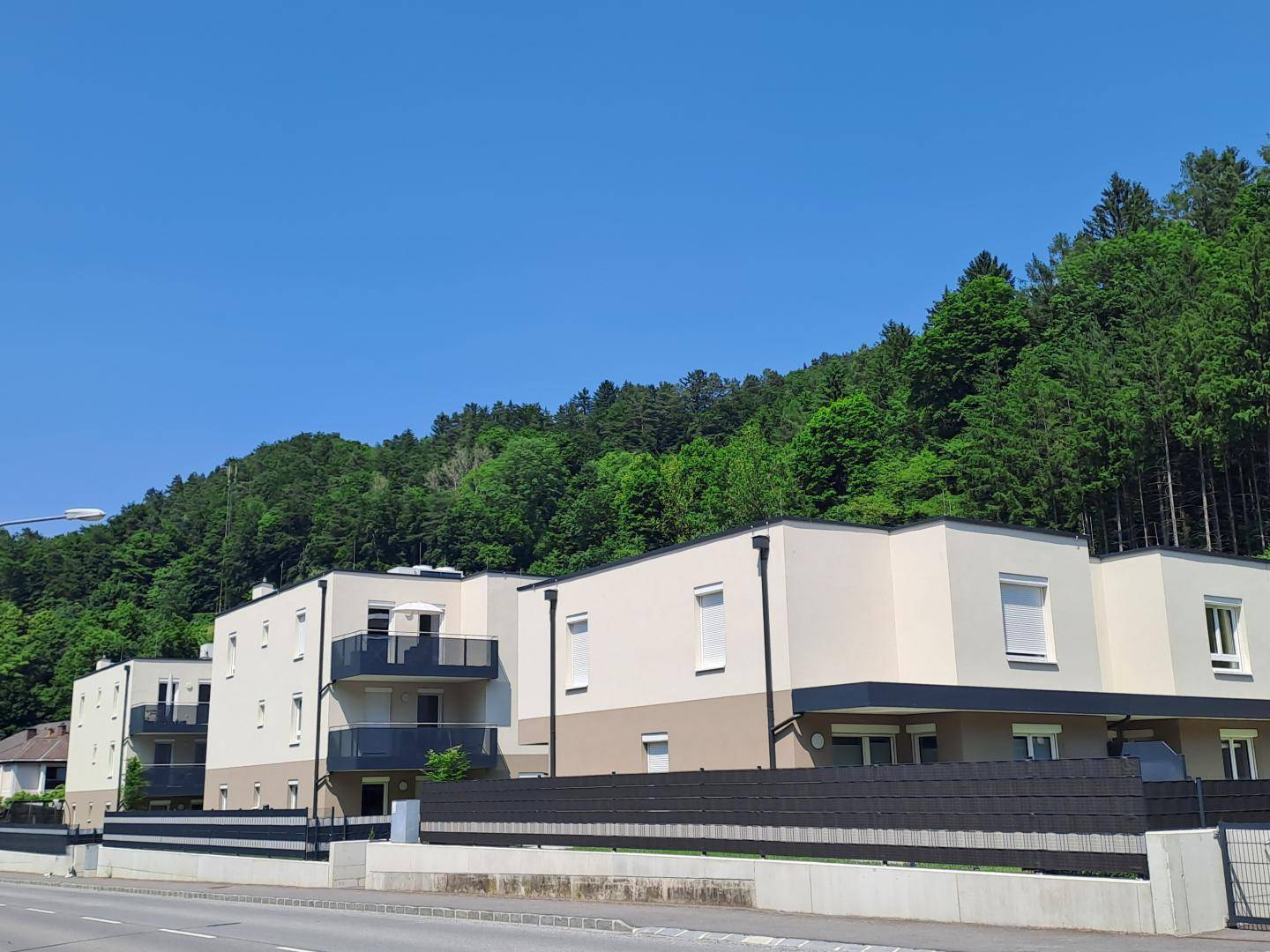 Moderne Wohngebäude mit Balkonen vor einer grünen, bewaldeten Hügellandschaft.