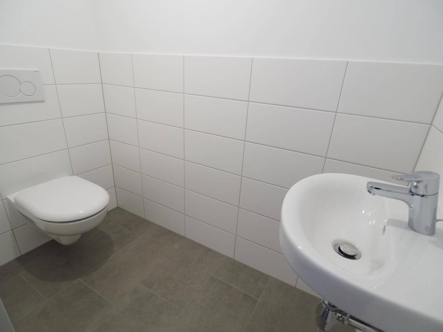 Modernes Gäste-WC mit weißen Fliesen, wandhängendem WC und kleinem Waschbecken.