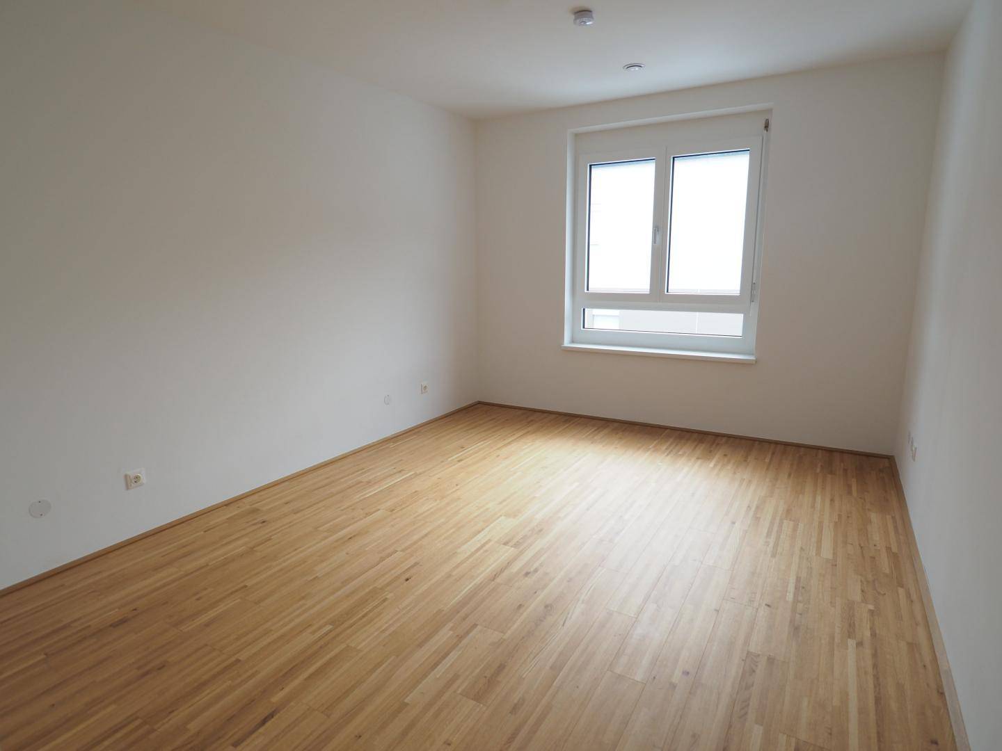 Helles Schlafzimmer mit Parkettboden und großem Fenster, bereit zur individuellen Gestaltung.
