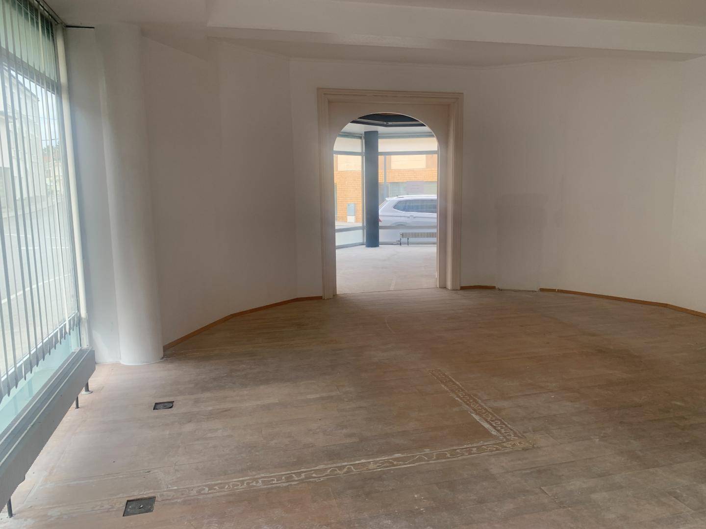Heller Raum mit Holzboden und einem eleganten Rundbogen, der zu einem weiteren Bereich führt.