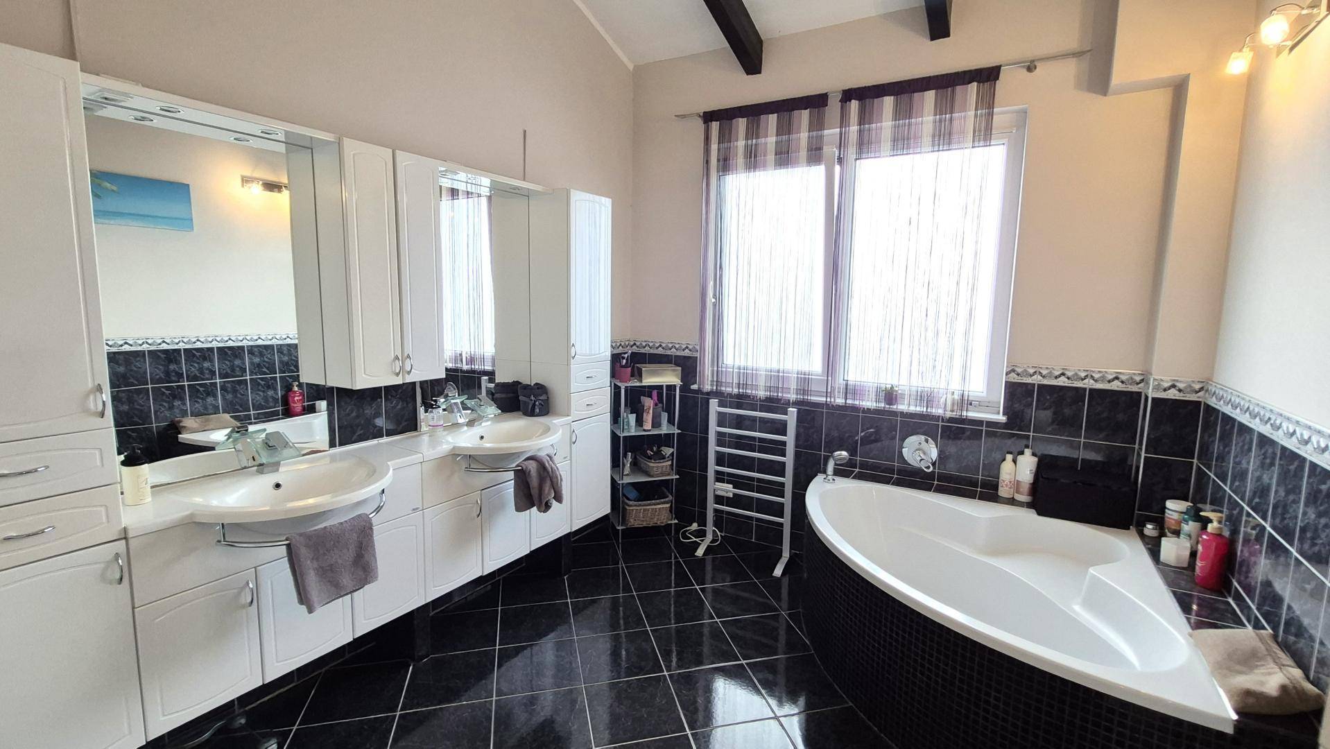 Geräumiges Badezimmer mit Doppelwaschbecken, Eckbadewanne und dunklen Fliesen.