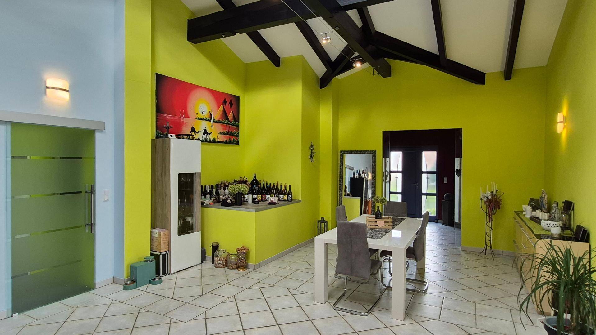Geräumiger Essbereich mit hohen Decken, sichtbaren Holzbalken und auffälligen grünen Wänden.