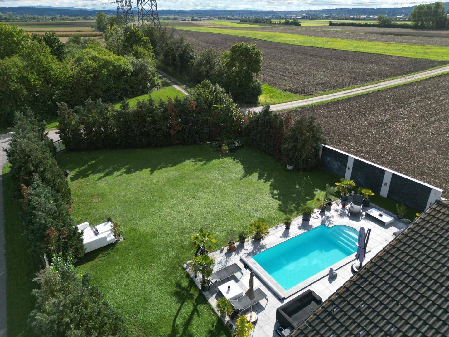 Luftaufnahme des weitläufigen Gartens mit Poolbereich und angrenzenden Feldern.
