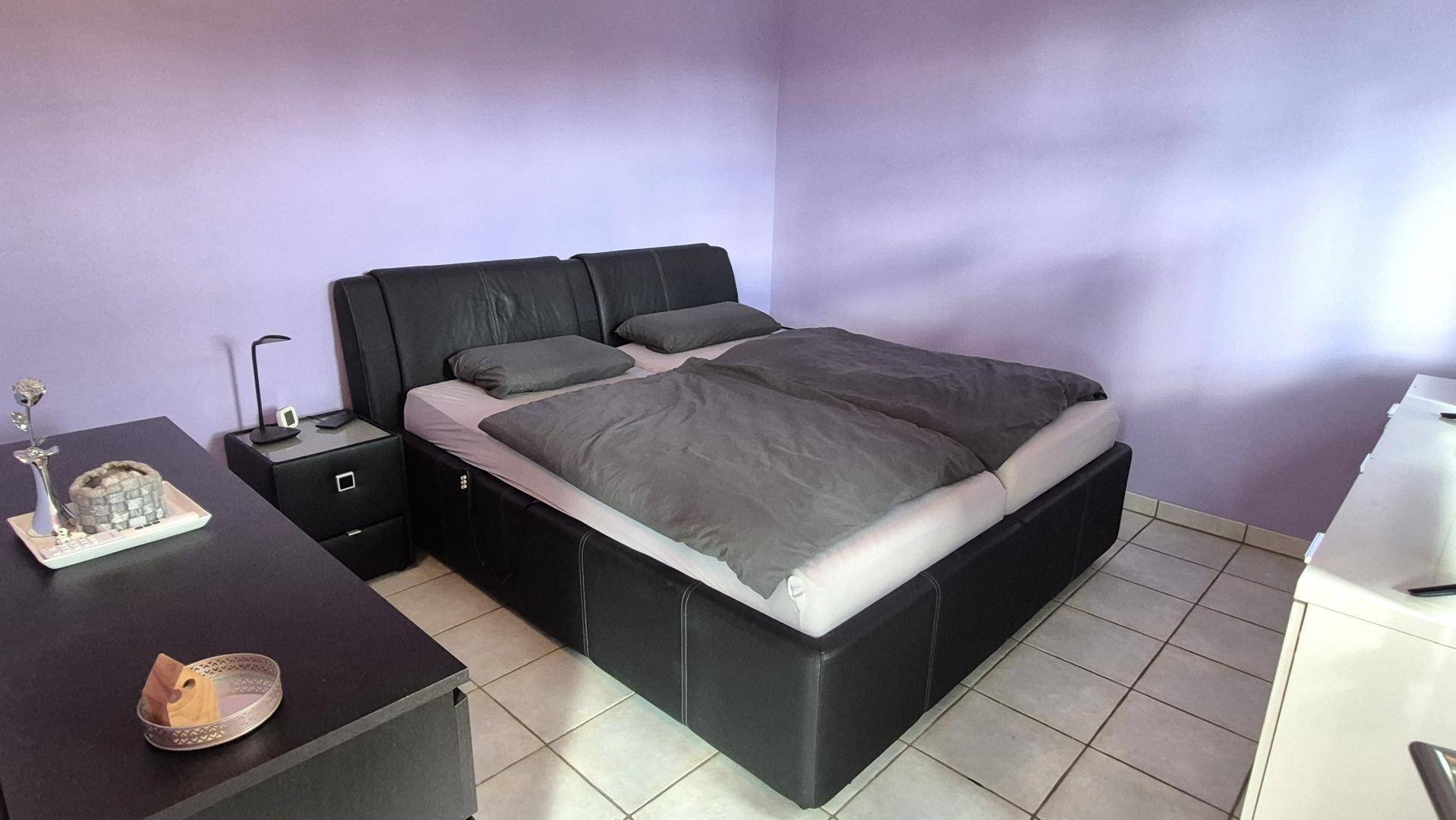 Schlafzimmer mit modernem Doppelbett, Nachttischen und lila gestrichenen Wänden.