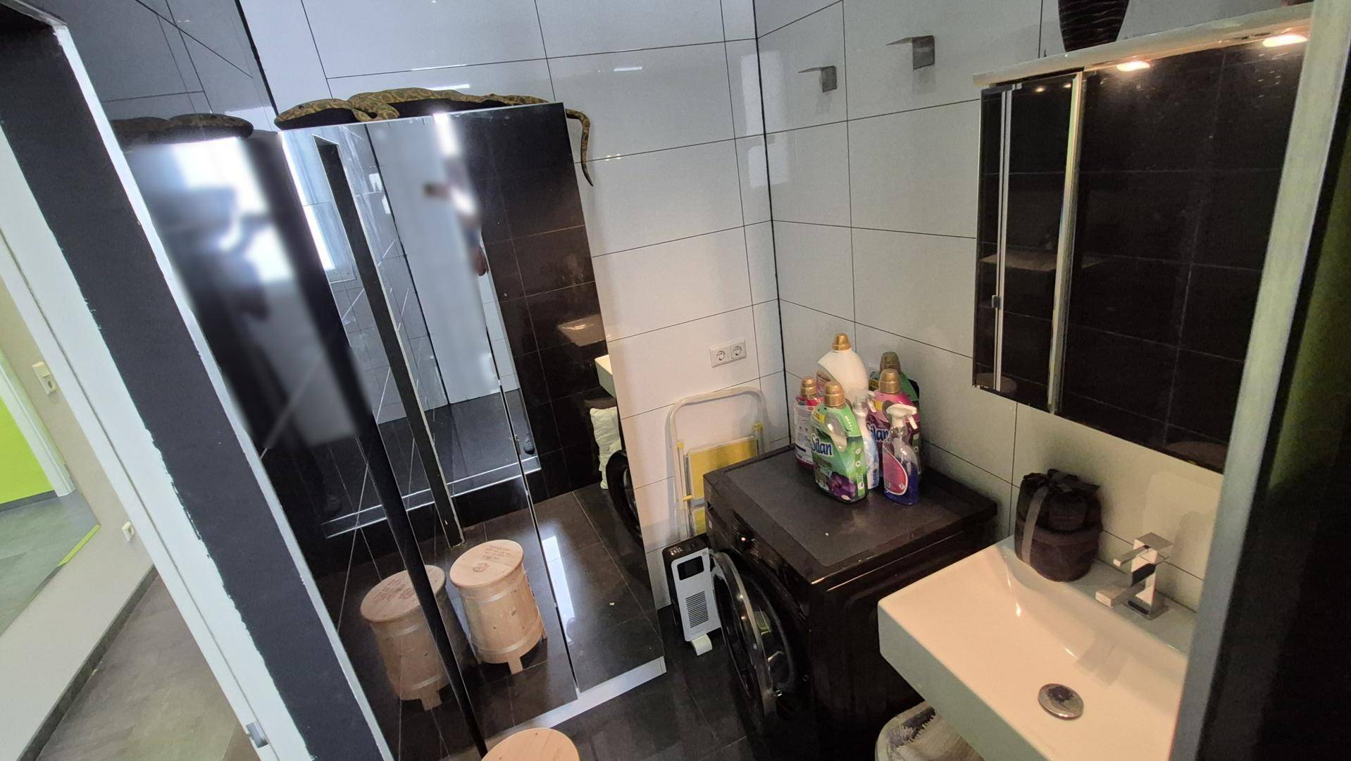 Kleiner Waschraum mit Waschmaschine, Waschbecken und dunklen Fliesen.