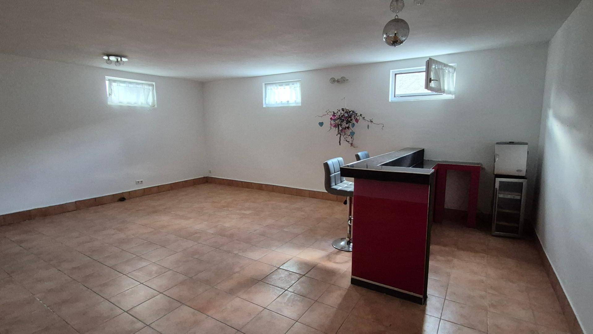 Großer Kellerraum mit kleiner Bar, Fliesenboden und Fenstern für Tageslicht.