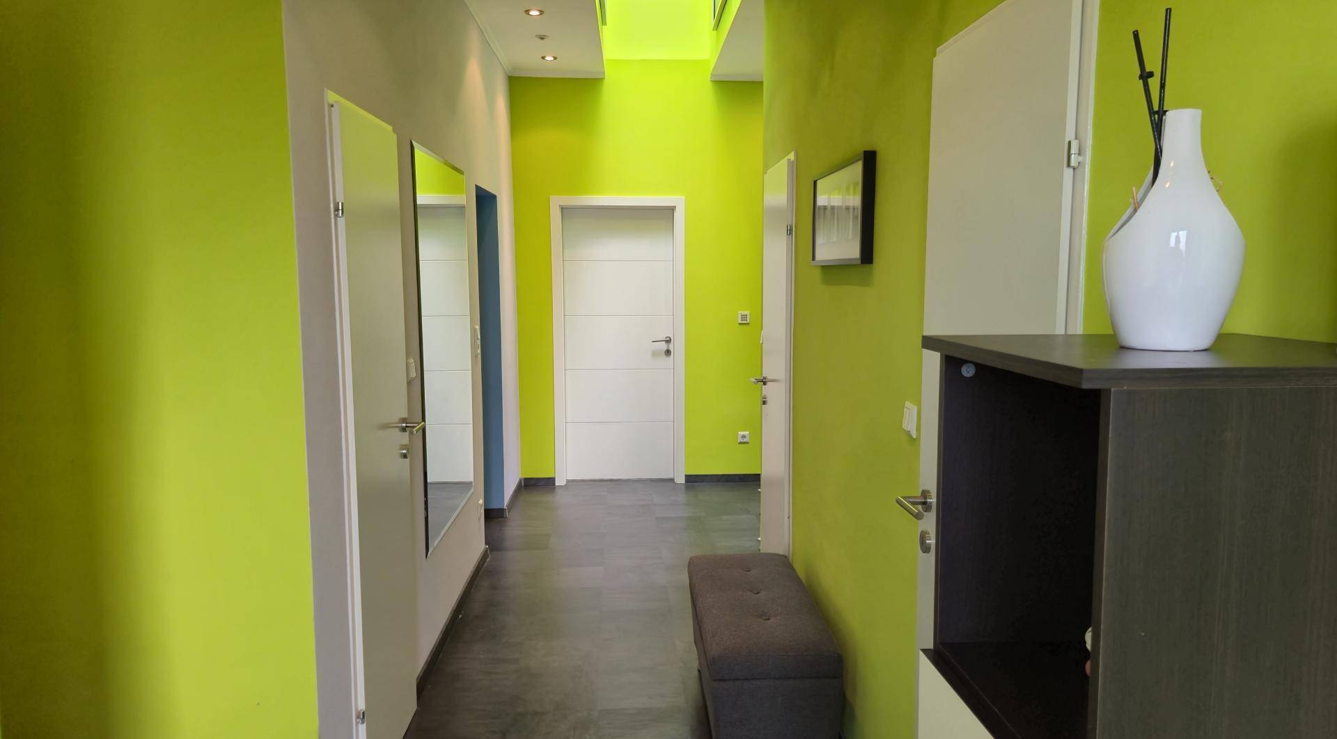 Langer Flur mit leuchtend grünen Wänden, Spiegeltüren und modernem Design.