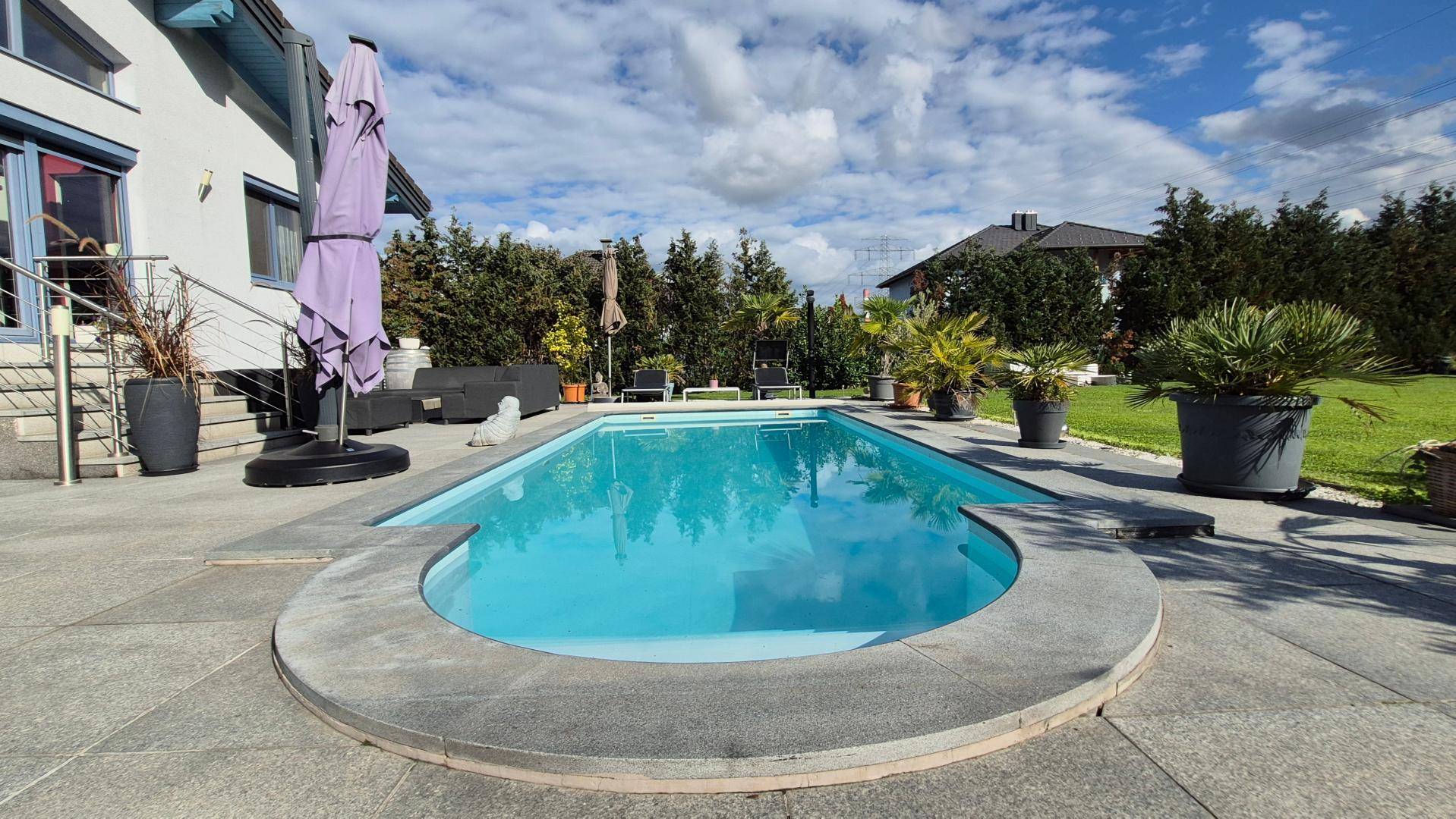 Großer Poolbereich mit gepflasterter Terrasse und üppiger Bepflanzung.