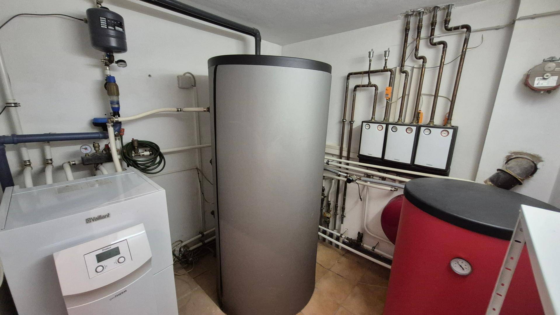 Technikraum mit Heizungsanlage, Warmwasserspeicher und sichtbaren Rohrleitungen.