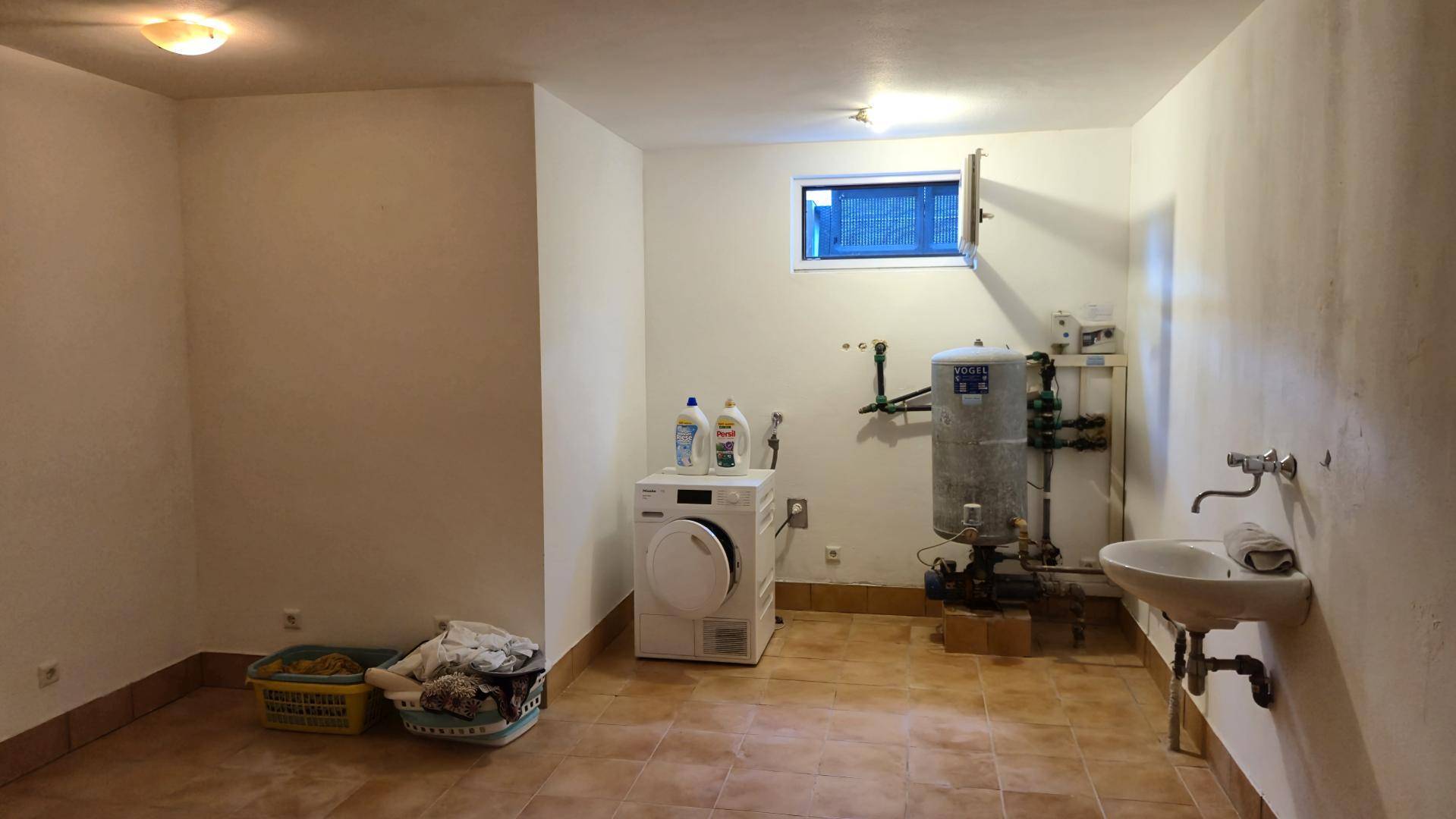 Heller Waschraum im Keller mit Waschmaschine, Waschbecken und Fenster.