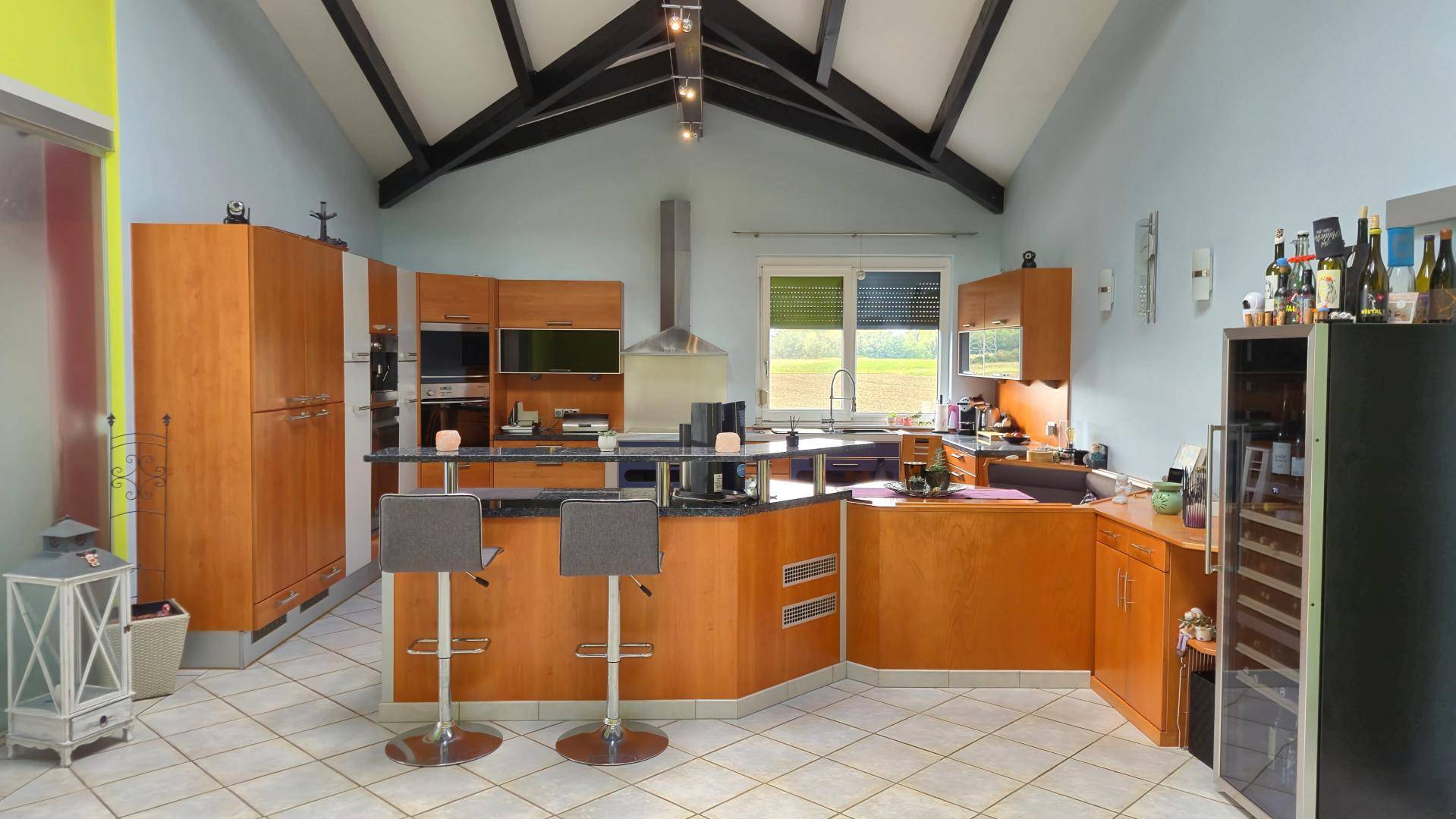 Geräumige Küche mit Holzelementen, Frühstücksbar und integriertem Essbereich unter hohen Decken.