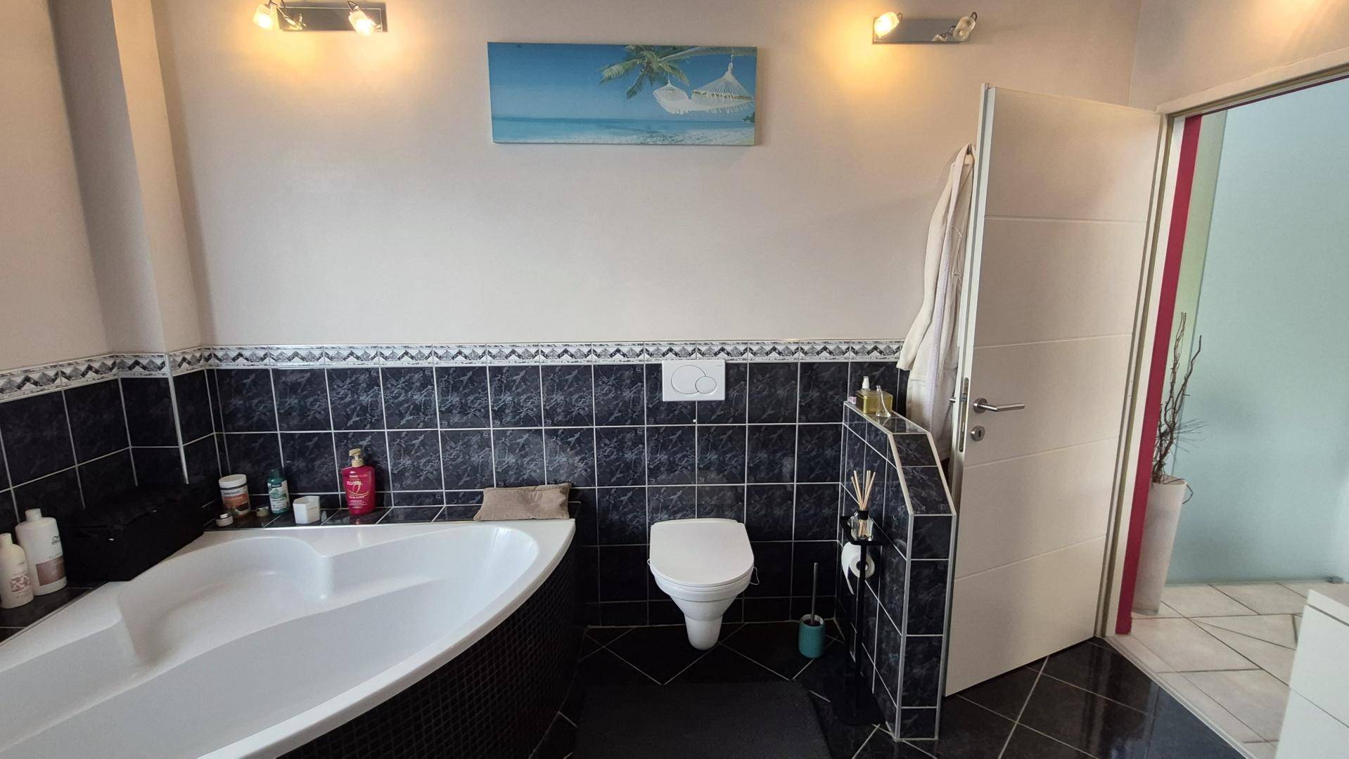 Badezimmer mit Eckbadewanne, Toilette und dunklen Fliesen, gut beleuchtet.